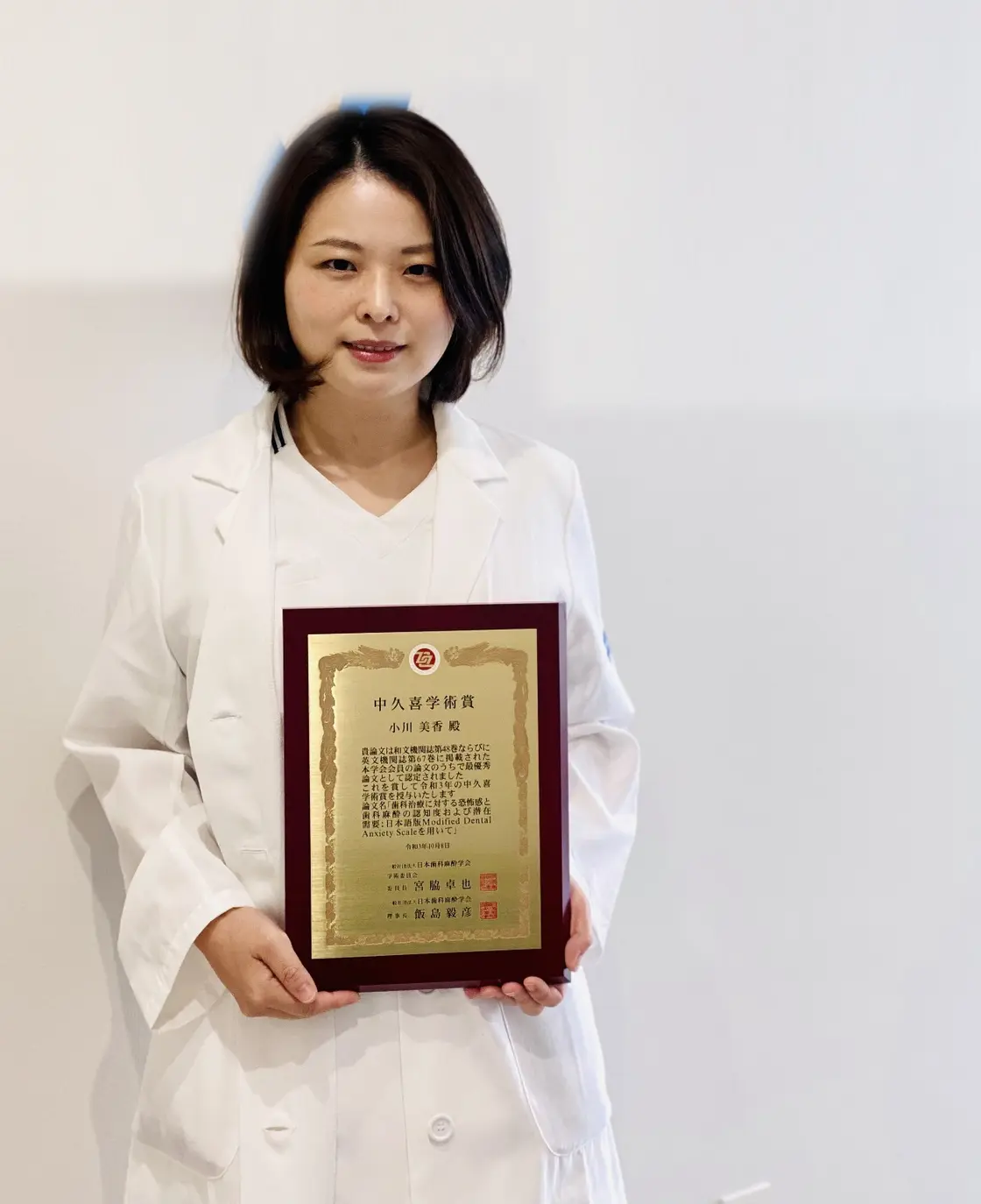 白衣で中久喜学術賞の受賞盾を持つ梶田美香。過去勤務先の背景表示は除去済み。